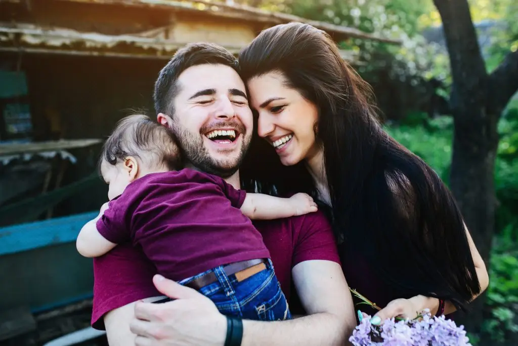 Papá y mamá abrazan a su bebe. Se ve una familia feliz